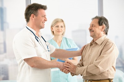 Smiling medical doctor shaking hands with happy senior patient, nurse in background.
